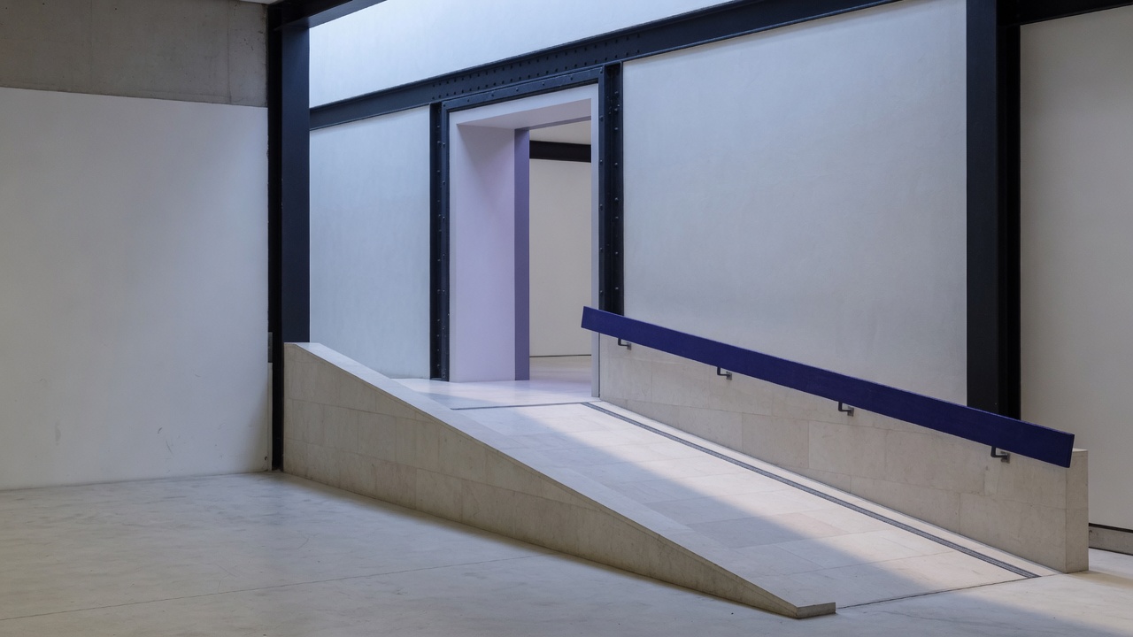 A pale stone ramp and indigo handrail leading through a cool white architectural doorway