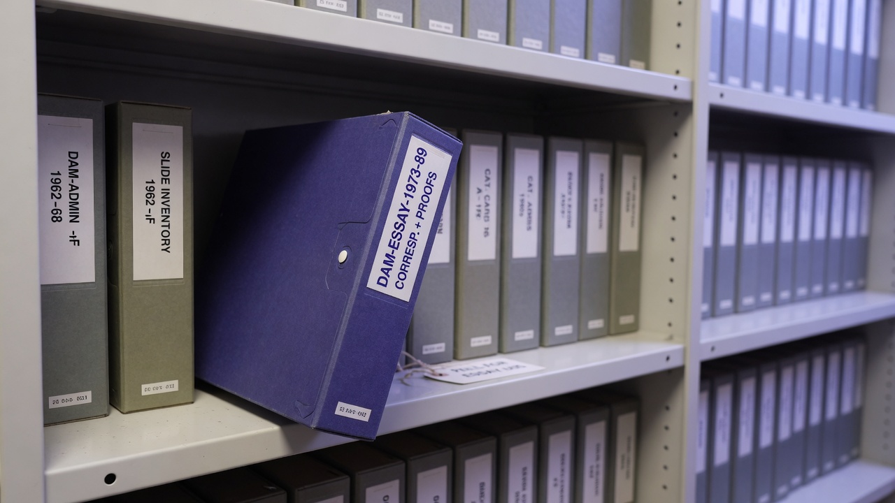 Archive boxes on a shelf with one indigo spine stepped forward