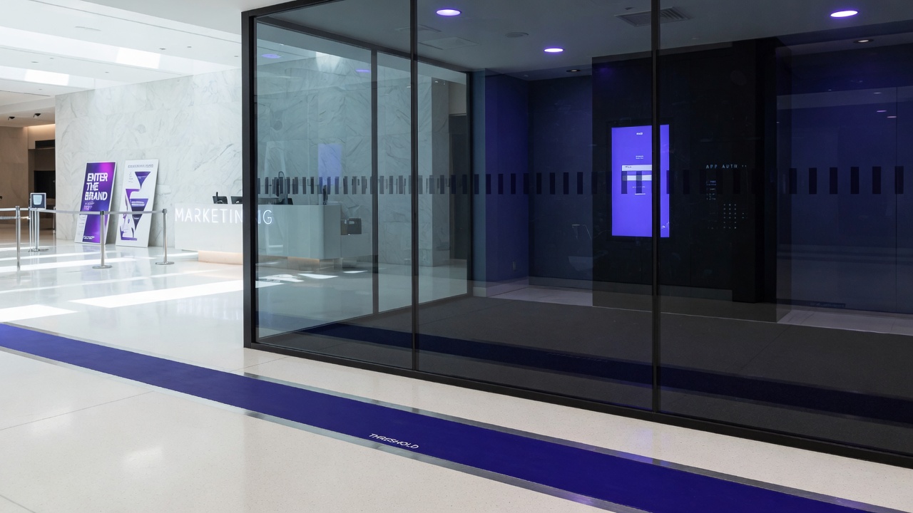 Glass wall dividing bright lobby from darker interior with indigo threshold