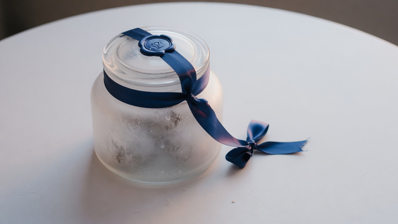 Frosted glass jar sealed with an indigo ribbon on a white table