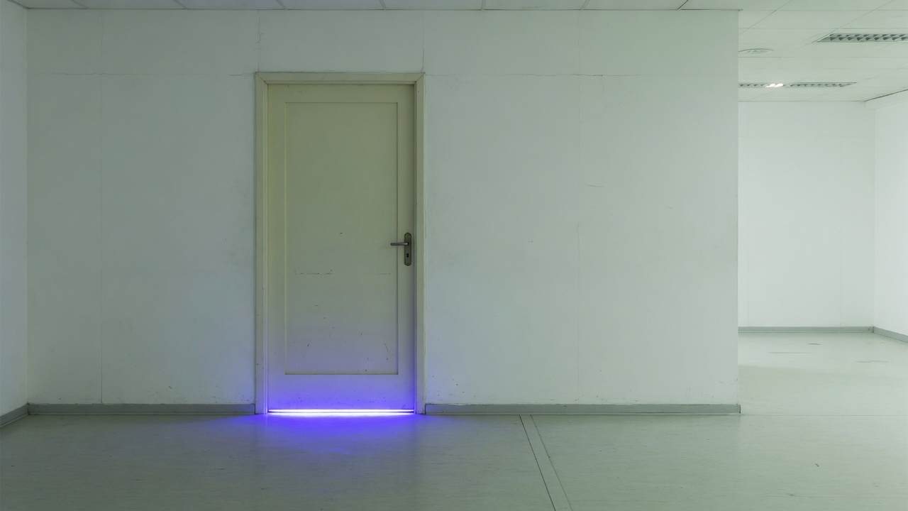 Pale door with indigo light under the gap in an empty white hall